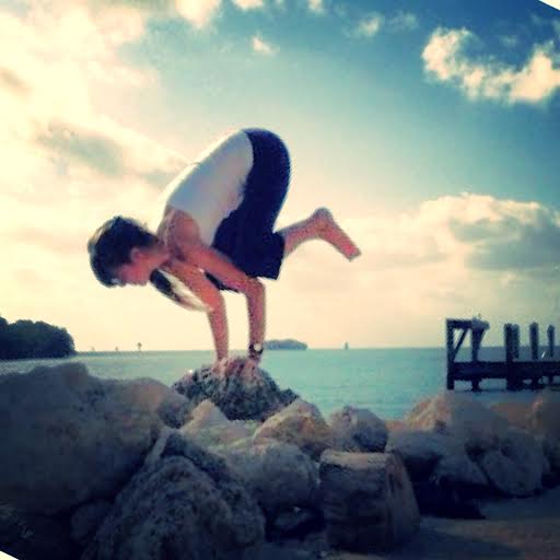 Person practicing yoga balancing on rocks near the ocean at sunset.