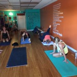 Group yoga session with participants in various poses on mats in a studio.