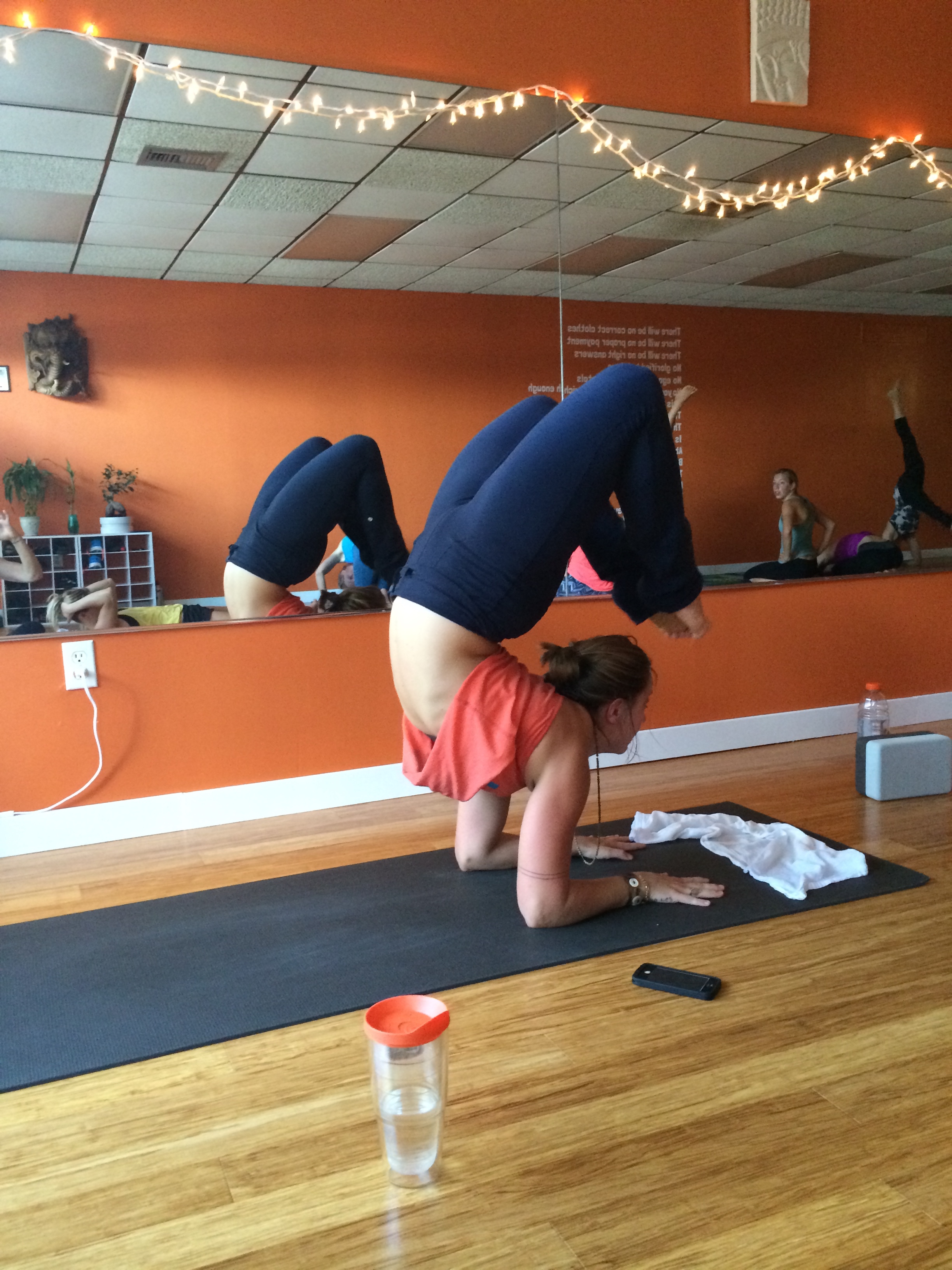 Person practicing advanced yoga pose in a mirrored studio.