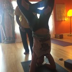 Person doing a headstand yoga pose indoors with others nearby.