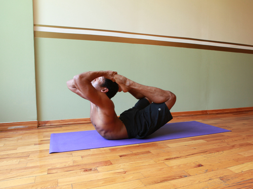 Man performing an advanced yoga pose on a mat indoors.