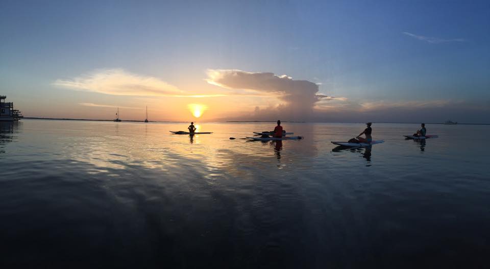 Silhouettes of kayakers at sunset on calm water.