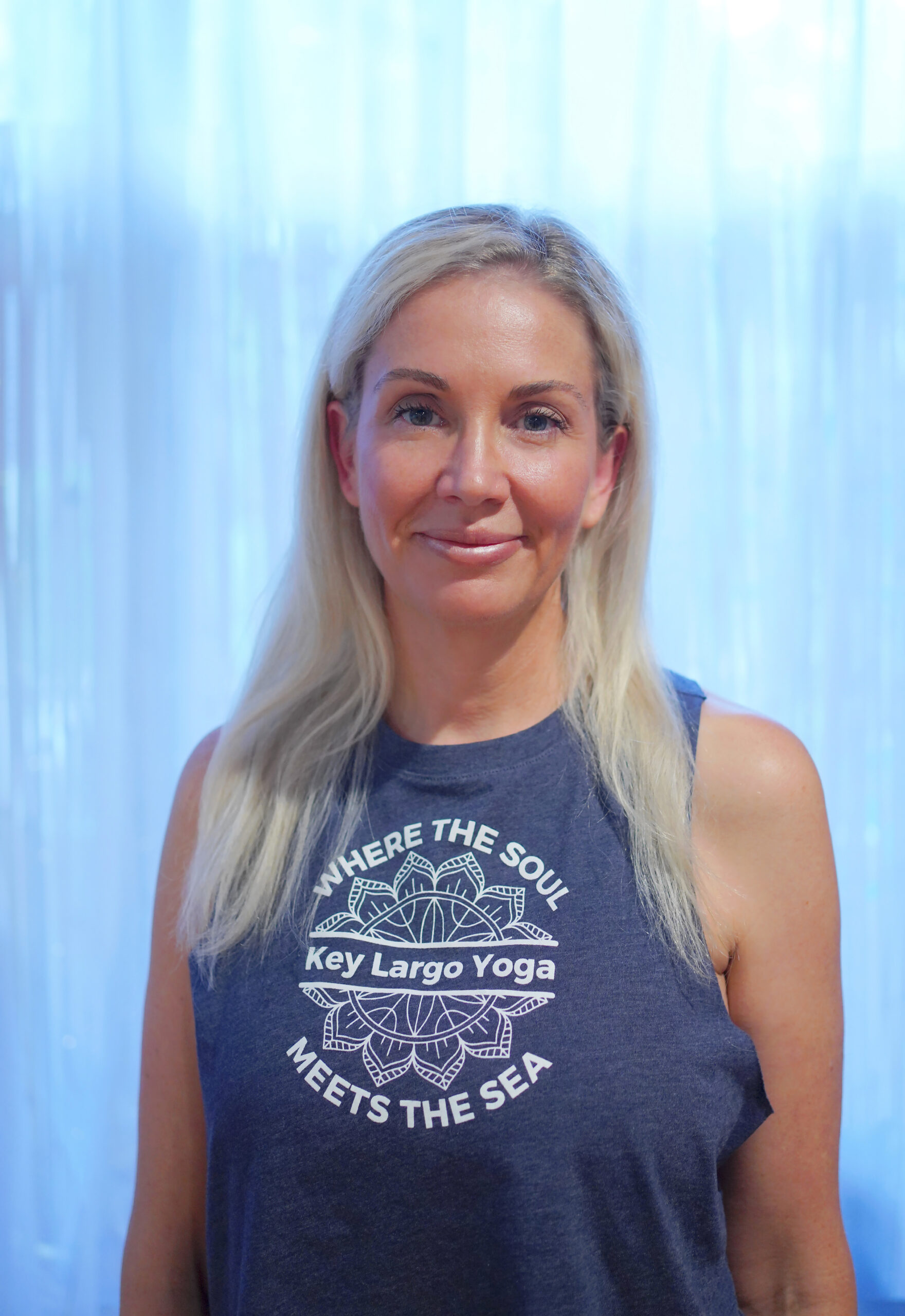 Smiling woman with long blonde hair wearing a sleeveless top.