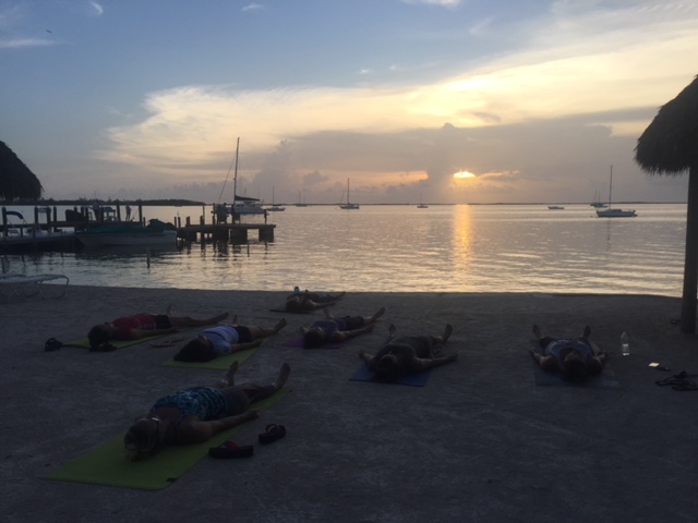 Sunset over a calm beach with scattered lounge chairs.