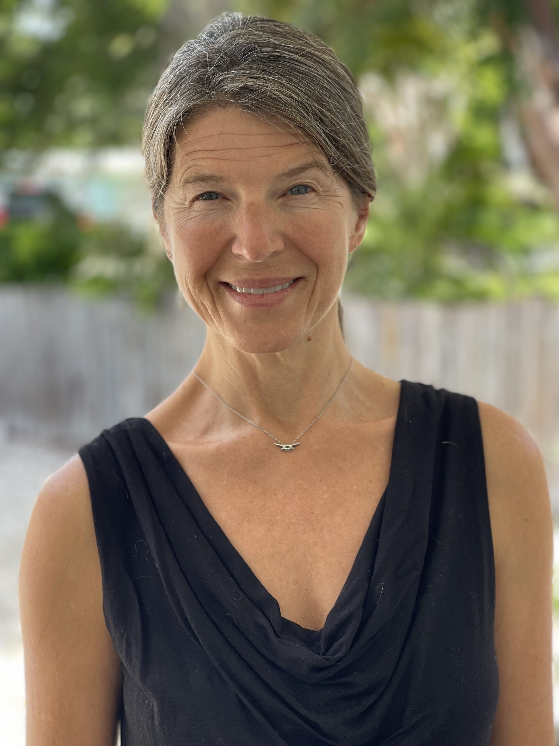 Smiling woman with gray hair in a sleeveless black top outdoors.